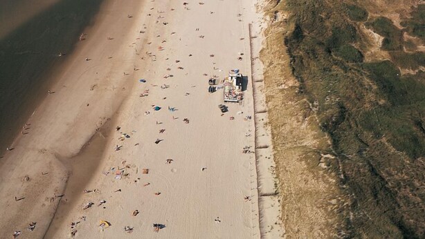 Luftaufnahme eines Strandes mit weitem Sandstreifen, einigen Personen und Strandsonnenschirmen.