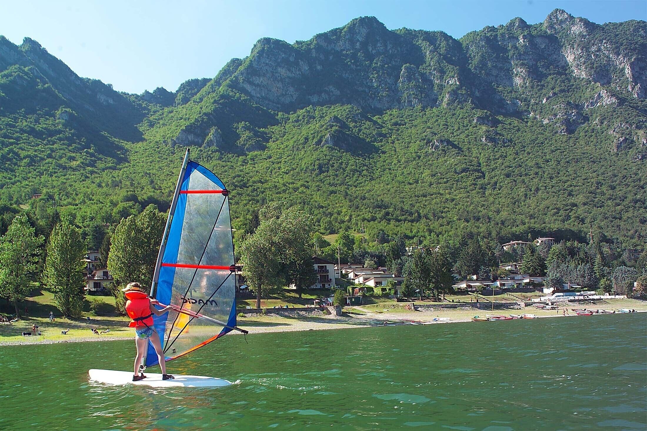A person windsurfing on a calm lake with mountains in the background.