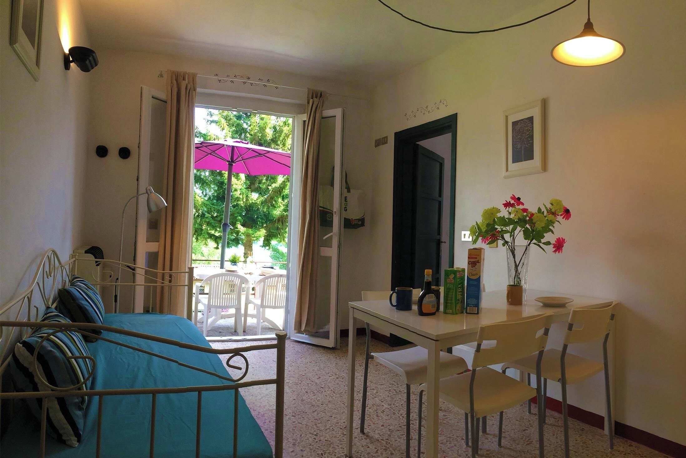A room with a bed, a table with chairs, a window with curtains, and a door.