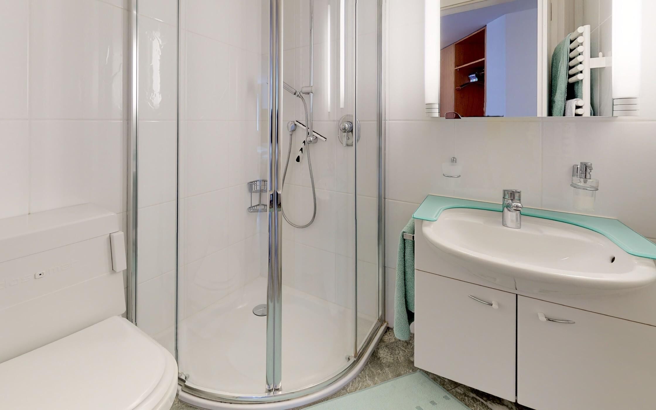 A modern bathroom with a glass-enclosed shower, a white sink with a green countertop, and a white toilet.