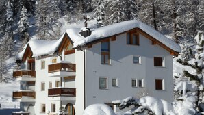 A multi-story hotel with balconies and a snow-covered roof, surrounded by trees. - Traditional nice apartment house in good location. (Celerina/Schlarigna)