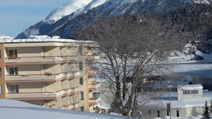 Un immeuble à plusieurs étages doté de balcons, entouré de montagnes enneigées.