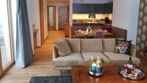 Uma sala de estar moderna com sofá, mesa de centro com velas e uma garrafa, e um espaço de jantar com mesa posta para dois.