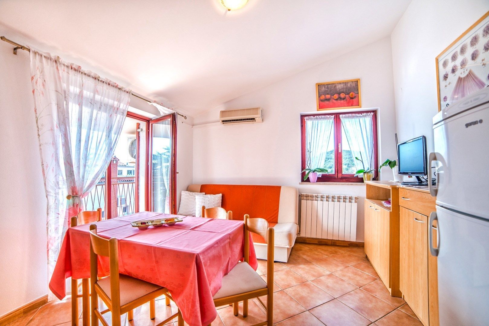 A compact kitchen with a dining area, a refrigerator, and a window with curtains.
