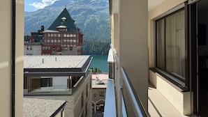 Un balcon avec vue sur les montagnes, un immeuble à la façade rouge et un ciel dégagé.
