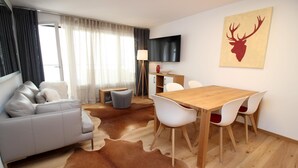 Un salon moderne avec un canapé gris, une table à manger en bois avec des chaises blanches, un téléviseur à écran plat et un tapis en peau de vache.