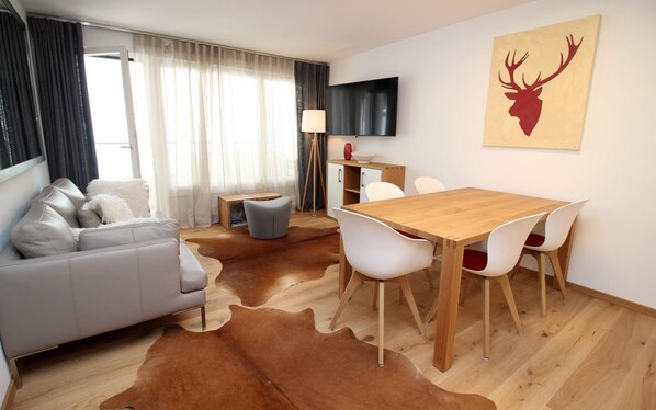 A modern living room with a grey sofa, a wooden dining table with white chairs, a flat-screen TV, and a cowhide rug. - The traditional residential building "Au Reduit" is located in the heart of St. (St. Moritz)