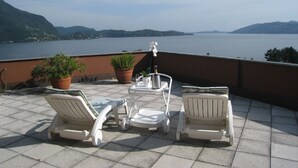A terrace with two white lounge chairs, a small table, and potted plants. - Studio with a breathtaking view of Lake Maggiore, incl. 1 PP Ged. (Ghiffa Verbania)