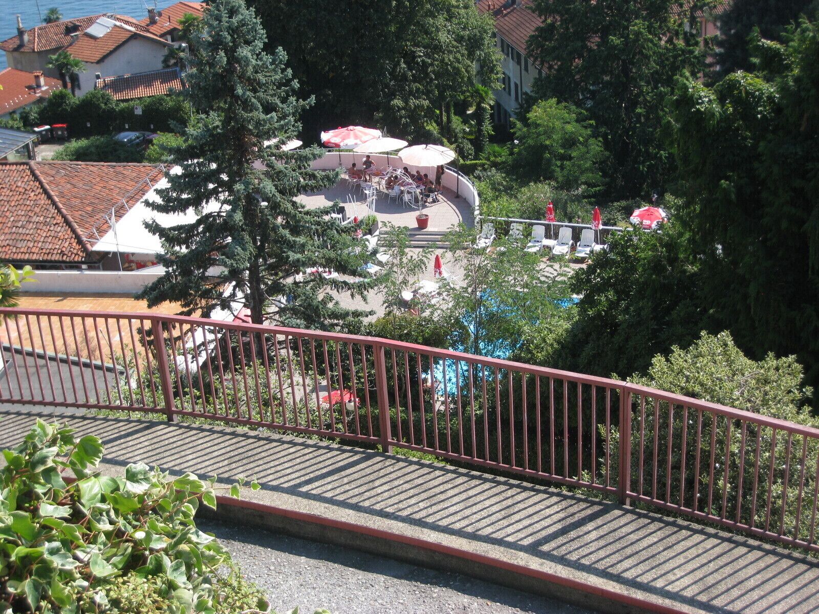 A view of a pool area with lounge chairs and umbrellas, surrounded by trees and buildings. - Studio with a breathtaking view of Lake Maggiore, incl. 1 PP Ged. (Ghiffa Verbania)