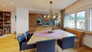 A modern dining area with a large wooden table, blue chairs, and a unique antler chandelier. - Apartmenthouse house next to the lake in St. (St. Moritz)