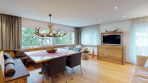 A modern living room with a wooden dining table, dark chairs, a sofa, and a TV on a wooden cabinet. - Apartmenthouse house next to the lake in St. (St. Moritz)