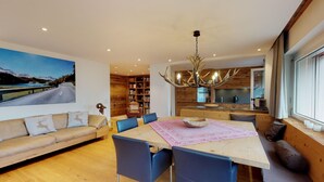 A modern living room with a large painting, a dining area with a wooden table, blue chairs, and a chandelier. - Apartmenthouse house next to the lake in St. (St. Moritz)