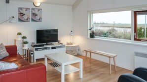 A modern living room with a flat-screen TV, a red sofa, a white coffee table, and a window with a view of a field.