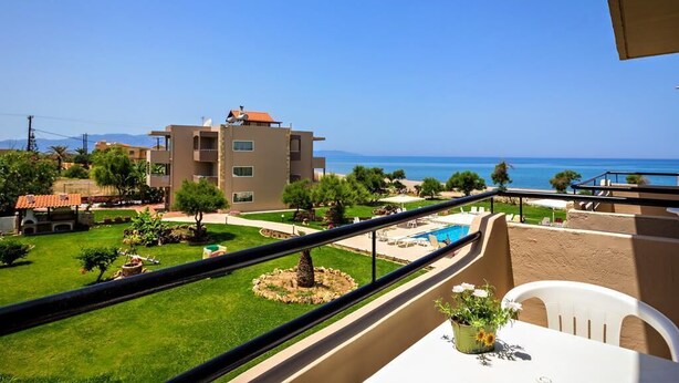 A balcony with a view of the sea, a pool, and a building with a red roof. - Matzi Apartments (Platanias)