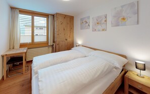 A bedroom with a wooden bed, a desk, and a chair. There are three paintings on the wall.