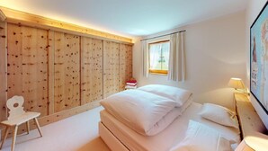 A bedroom with a wooden wardrobe, a bed with white linens, a small desk, and a window with curtains. - The traditional Chesa Marmotta is situated next to the famous River "Inn" in a v (Celerina/Schlarigna)