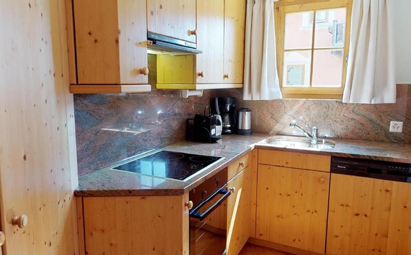 Cuina amb armaris de fusta, taulell de granat i forn de murri, cafetera i finestra amb cortines.