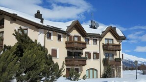 A multi-story building with balconies, a snow-covered roof, and a mountainous backdrop. - The traditional Chesa Marmotta is situated next to the famous River "Inn" in a v (Celerina/Schlarigna)