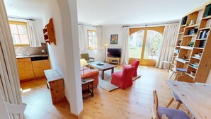 A spacious living area with a wooden floor, a dining table, red chairs, a TV, and a bookshelf. - The traditional Chesa Marmotta is situated next to the famous River "Inn" in a v (Celerina/Schlarigna)