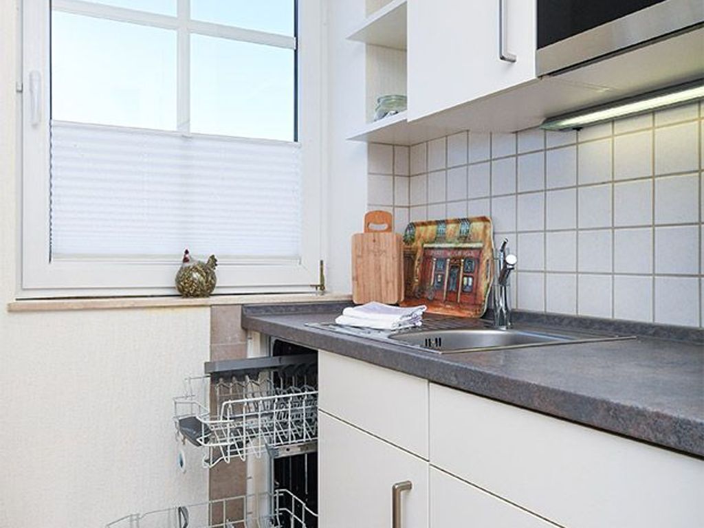 A kitchen with a dishwasher, a window with blinds, a sink, and a tiled backsplash.