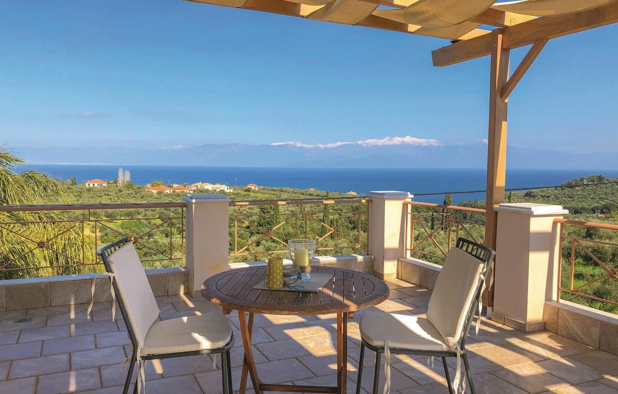 Eine Terrasse mit rundem Tisch und Stühlen, mit Blick auf eine malerische Landschaft mit Bergen und dem Meer.