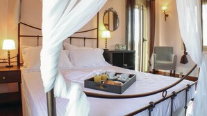 Una cama con dosel con una bandeja de desayuno, una lámpara de noche, un espejo y una silla en una habitación de hotel.