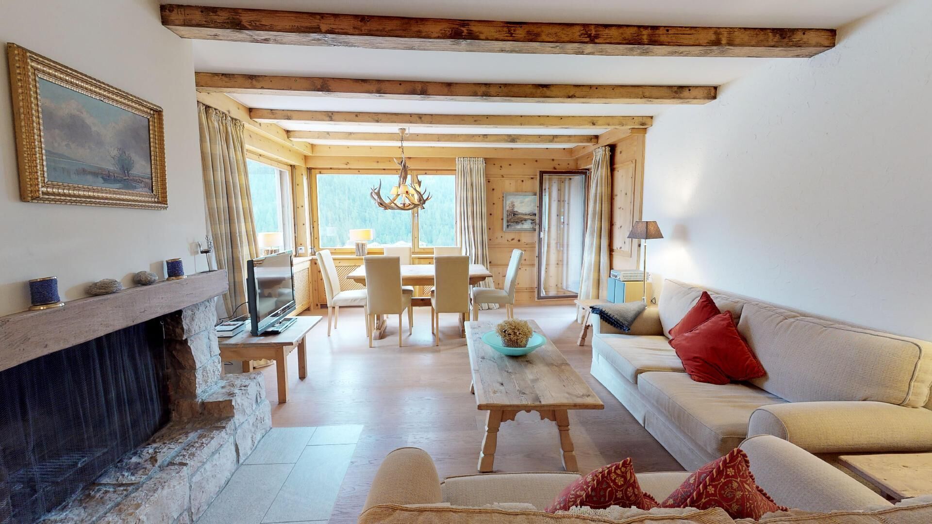 Ein gemütliches Wohnzimmer mit Kamin, Holzbalken, Essbereich und einer Couch mit roten Kissen.