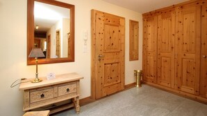 Un couloir avec des portes en bois, un miroir, une coiffeuse avec une lampe et une petite table.