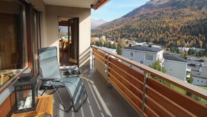 Un balcon donnant sur un paysage montagneux, une chaise et une table avec une lanterne.
