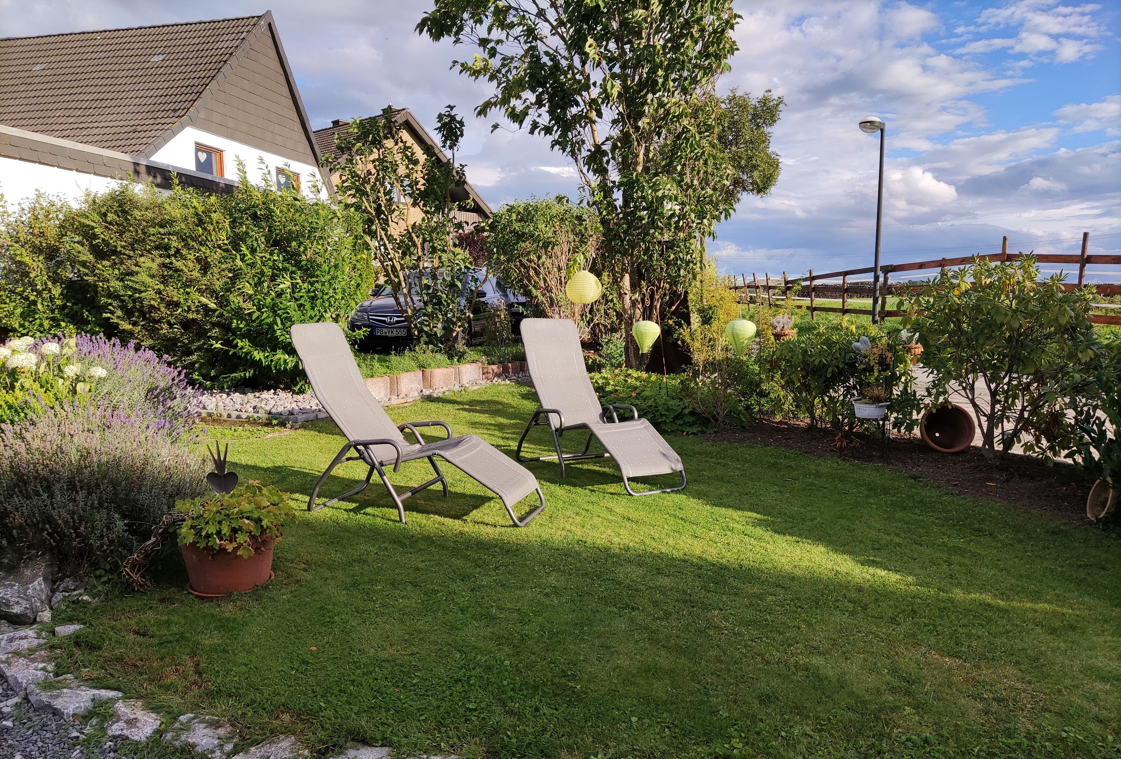 Ein Garten mit zwei Liegestühlen, einem Kiesweg und verschiedenen Pflanzen.