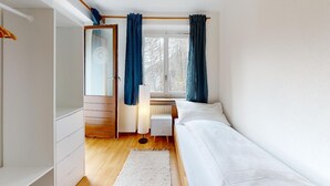 Ein Schlafzimmer mit Bett, Nachttisch, Kleiderschrank und einem Fenster mit Vorhängen.