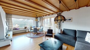Ein geräumiger Wohnbereich mit Holzbalkendecke, einer Couch, einem Couchtisch und einem Esstisch mit Stühlen.