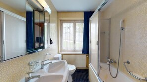Une salle de bain avec deux lavabos, des toilettes, une douche et une fenêtre avec des rideaux.