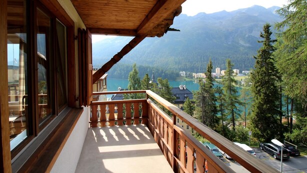Ein Balkon mit Holzgeländer, der auf eine gebirgige Landschaft und einen See blickt.
