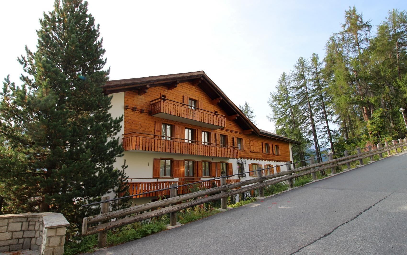 A multi-story wooden building with balconies, surrounded by trees.
