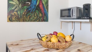 Ein Zimmer mit einem Holztisch, einer Fruchtkorb, einer Mikrowelle und einer Kaffeemaschine auf einem Regal.