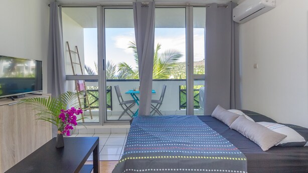 Ein Schlafzimmer mit Bett, Fernseher, Schreibtisch und einem Balkon mit Tisch und Stühlen.