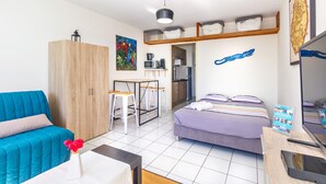 Ein kompaktes Hotelzimmer mit Bett, einer Sitzecke, Schreibtisch mit Stuhl, einer Küchenzeile und einem Fernseher.