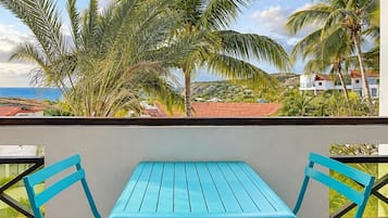Une table et des chaises en métal de couleur turquoise, sur un balcon offrant une vue sur des palmiers et une étendue d’eau.