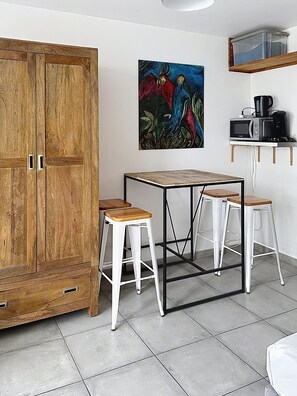 A compact kitchen with a wooden cabinet, a table with stools, and a microwave. - Boucan Beach - Nice studio sea view in Boucan Canot (St Gilles) (Boucan Canot)