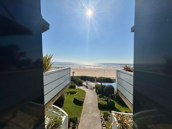 A view from a balcony overlooking a beach with a clear sky and a sun shining.