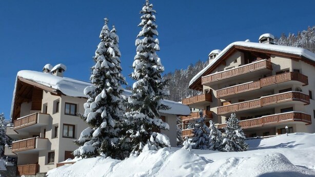 A snow-covered building with multiple balconies and a ski slope in the background. - Very well located apartment house in the area of Park-Salet. (St. Moritz)