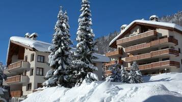 Ein mit Schnee bedecktes Gebäude mit mehreren Balkonen und einer Skipiste im Hintergrund.