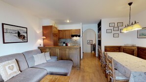 A cozy living room with a grey sofa, wooden coffee table, and a dining area with a table and chairs. A kitchen with wooden cabinets and a tiled backsplash is visible in the background. - Very well located apartment house in the area of Park-Salet. (St. Moritz)