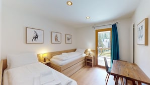 A room with two beds, a wooden table, and a chair. There are three framed pictures on the wall. - Very well located apartment house in the area of Park-Salet. (St. Moritz)