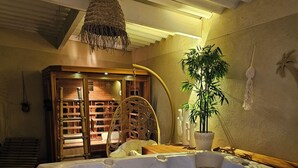 Un bain à remous avec un éclairage bleu, un fauteuil en osier, une plante en pot et une structure en bois dotée d’étagères.