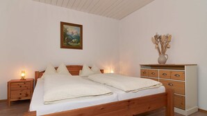 A wooden bed with two pillows, a nightstand with a lamp, a dresser with drawers, and a painting on the wall. - 02 Apartment Sonnleiten 35 sqm for max. 3 p., kitchen, 1 living/bedroom, 1 bedroom, balcony (Bergen)