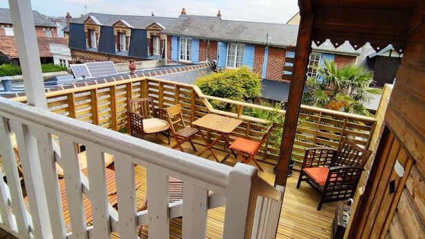 Een houten terras met buitenmeubilair, een zonnepaneel en uitzicht op woonhuizen.