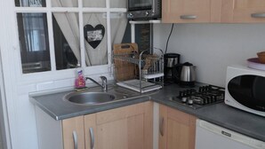 Een kleine keuken met een spoelbak, kookplaat, magnetron en houten kastjes.