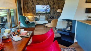 Ein modernes Wohnzimmer mit einer Couch, Sesseln, einem Fernseher und einem Kamin.